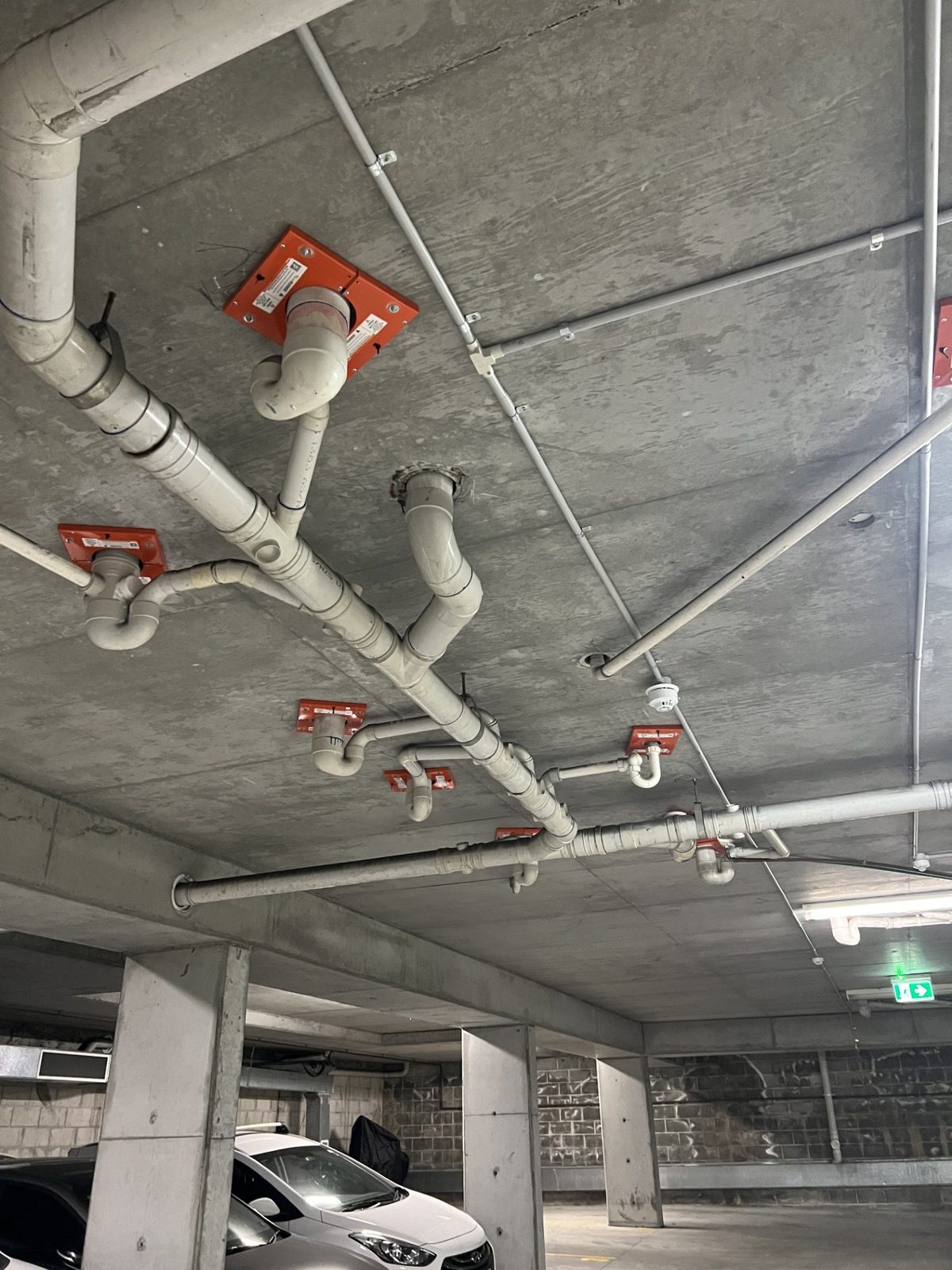 Intumescent fire collars on pipe penetrations through a concrete slab in an Inner West Sydney apartment building